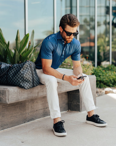 lifestyle image: man sitting outside airport with luggage, using phone.