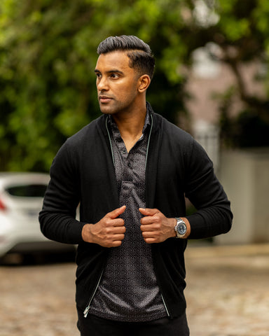 lifestyle image: man walking outside with black merino full zip jacket from Collars & Co. He is pulling the jacket tighter by gripping the zipper.