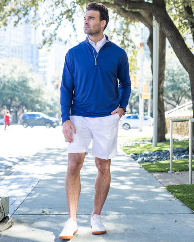 lifestyle image: man in shorts wearing a tour performance pullover from Collars & Co. outside on a sidewalk, near a tree. Wearing shorts.