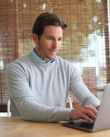 man wearing grey luxury touch cotton cashmere crew neck sweater preparing for performance review on laptop