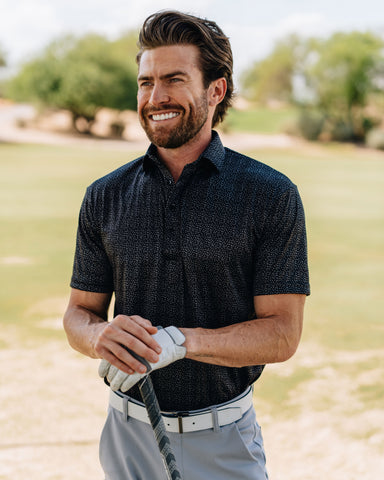 man with golf club wearing desert sky semi-spread collar polo, standing on golf course