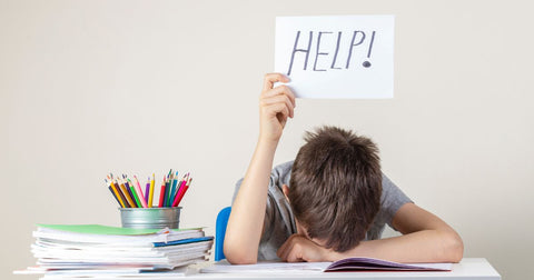 A young boy with head on table holding a sign saying help