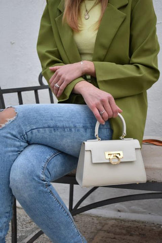 A woman in blue jeans is sitting, holding a carbotti handbag