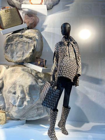 a black manequin in the same colored valentino black and white short coat, high boots and with a big tote bags by the large rocks art installation
