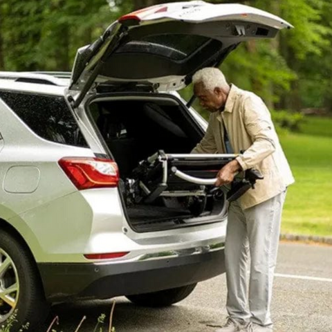 old man loading wheelchair in back of car