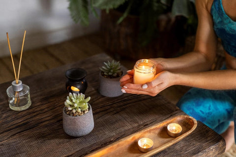 Woman holding a candle in a glass, with a diffuser and plant on the table