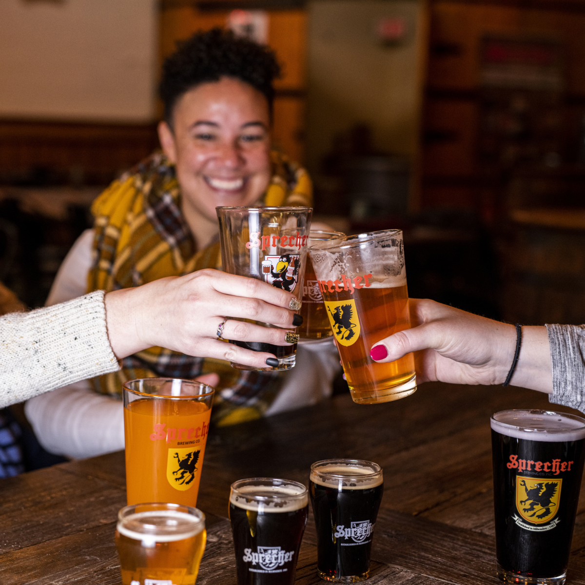 People cheersing sprecher beers and sodas in a taproom, smiling woman in the background.