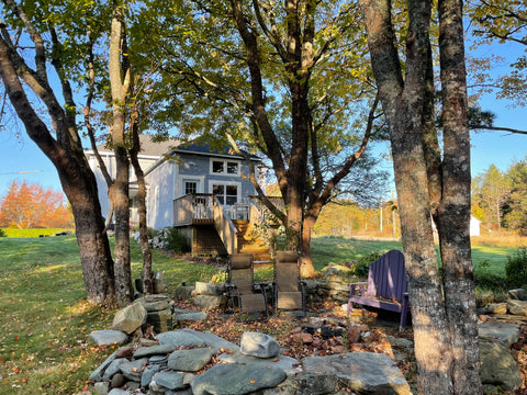 Outside view of the condo rental, with stairs out front leading to front door. Two lawn chairs and a wood bench in foreground, surrounded by trees.