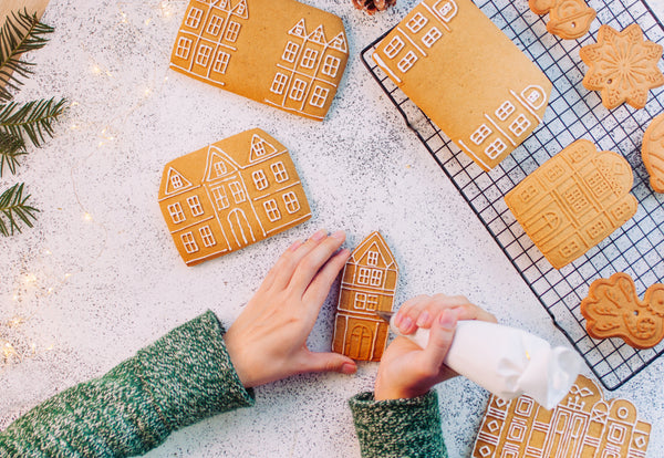 woman decorating gingerbread cookies to assemble into a house