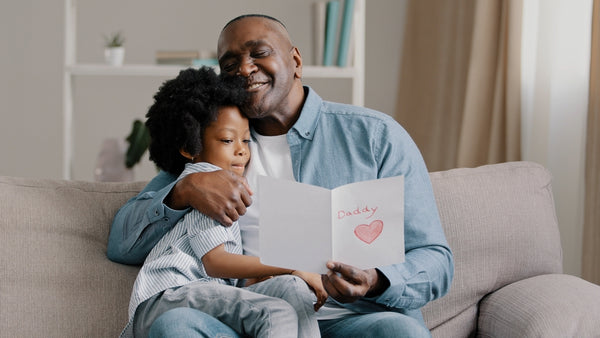 Black man and granddaughter sitting while reading a Happy Father’s Day card message together