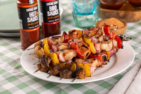 A plate of super skewers looking juicy and delicious with a bottle of DF Smoke Haus BBQ sauce and a bottle of Hot sauce in the background
