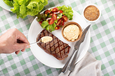 A plate of steak and garden salad, with a small wooden bowl of cowboy butter made with DF Smoke Haus Darling Downs Dust seasoning. A hand is putting a teaspoon of cowboy butter on top of the steak.