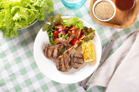 A plate of juicy barbecued lamb cutlets, grilled corn and garden salad.