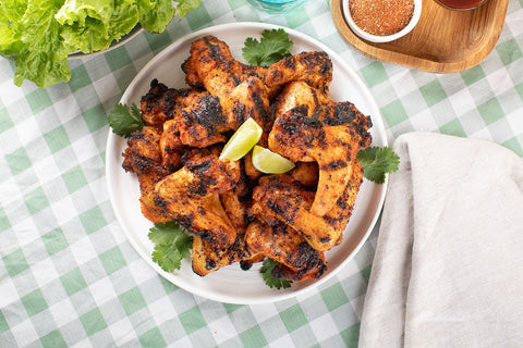 A plate of barbecued chicken wings piled high, looking crispy and delicious, with a lemon wedge on top.