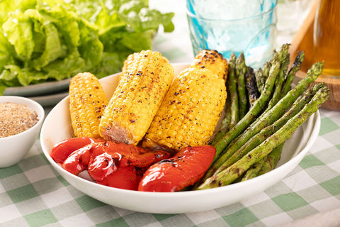 A bowl of chargrilled veggies, including cobs of corn, asparagus and red capsicum