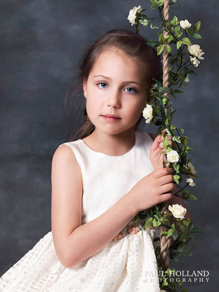 Fine Art Portrait by Paul showing a young girl holding the rope handle of a swing covered in flowers