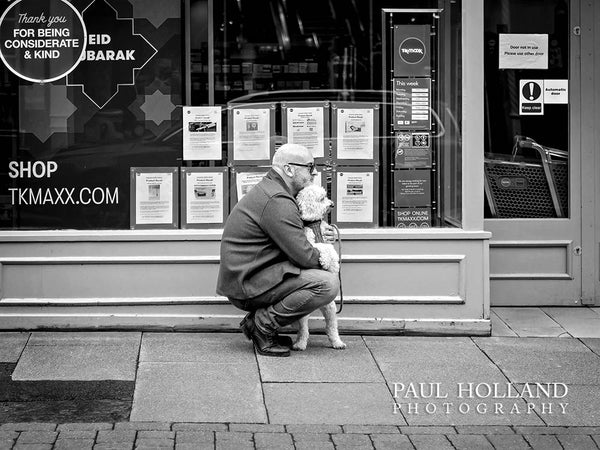 Black and white image shows a man and dog outside a shop