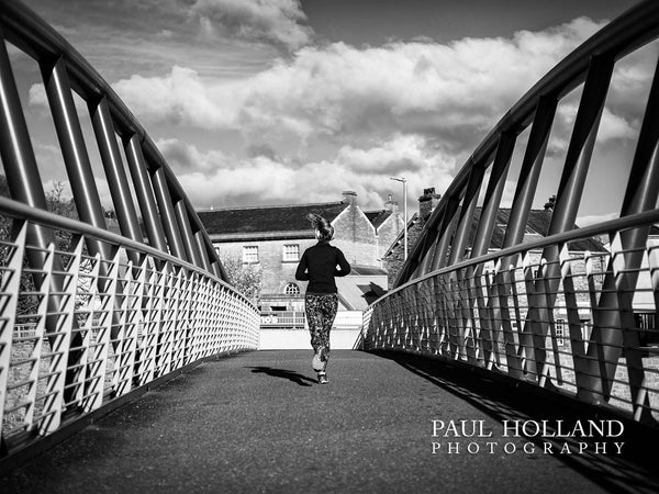 Black and white image shows a woman running across the bridge with symmetrical bridge structure on each side