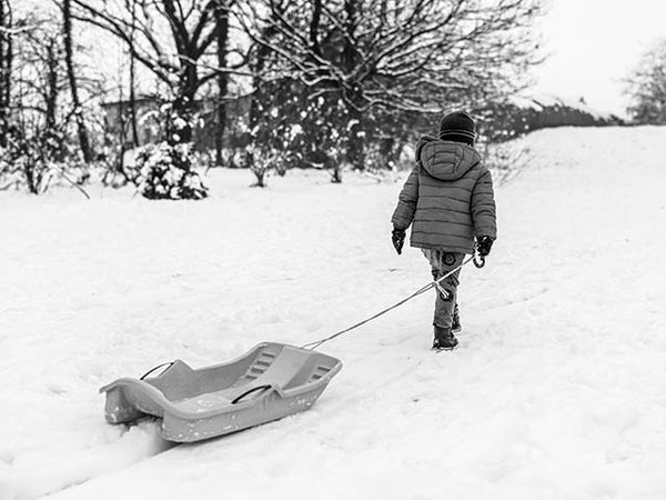 Black and white image showing a child dragging a sledge back up the hill