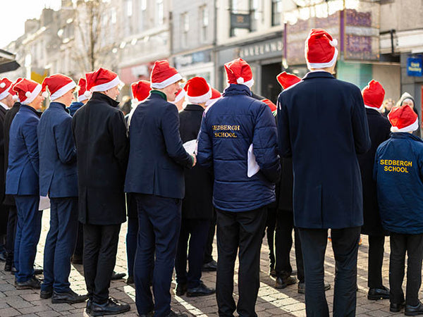 Image shows a group of carol singers wearing Santa hats