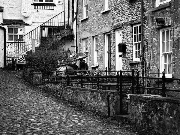 Black and white image showing a row of stone cottages with a motor scooter outside