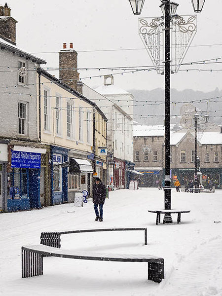 Image shows a man walking through the snow in Kendal Market Place