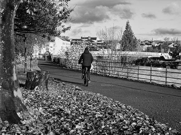 Black and white image shows a cyclist on the riverside path in Kendal