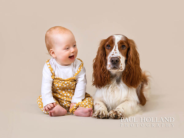 Image of a young toddler laughing while sitting alongside a dog