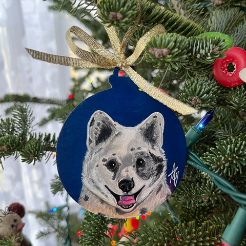 Acrylic painting of a white, grey, and tan dog on a dark blue background. The painting is on a Christmas ornament.