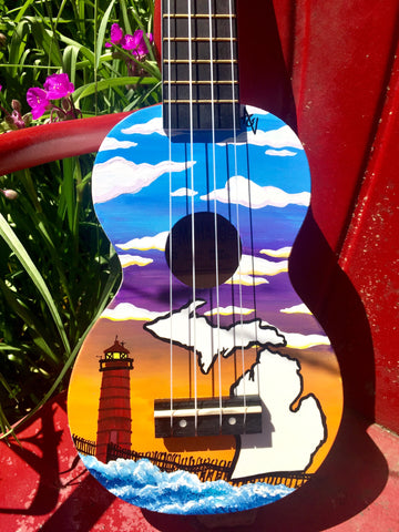 Hand painted ukulele depicting the Grand Haven light house against a sunset sky. A white silhouette of the state of Michigan is in the right lower quadrant.