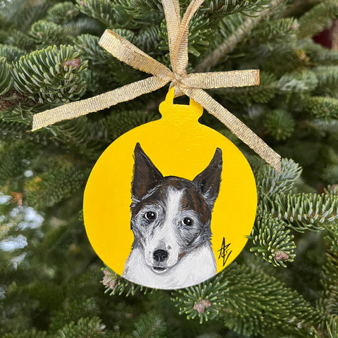 Acrylic painting of a brown and white dog with pointy ears against a yellow background, painted on a Christmas ornament.
