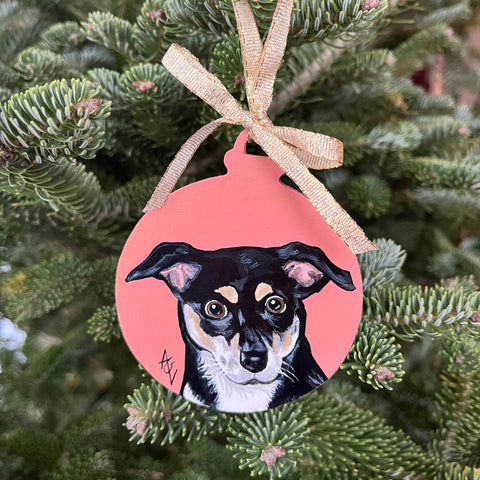 Acrylic painting of a black and white dog on a salmon colored background, painted on a Christmas ornament.