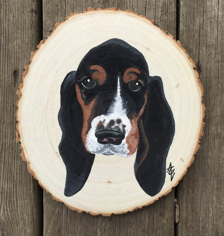 Acrylic painting on wood slice depicting the cute face of a black, white, and tan basset hound puppy.