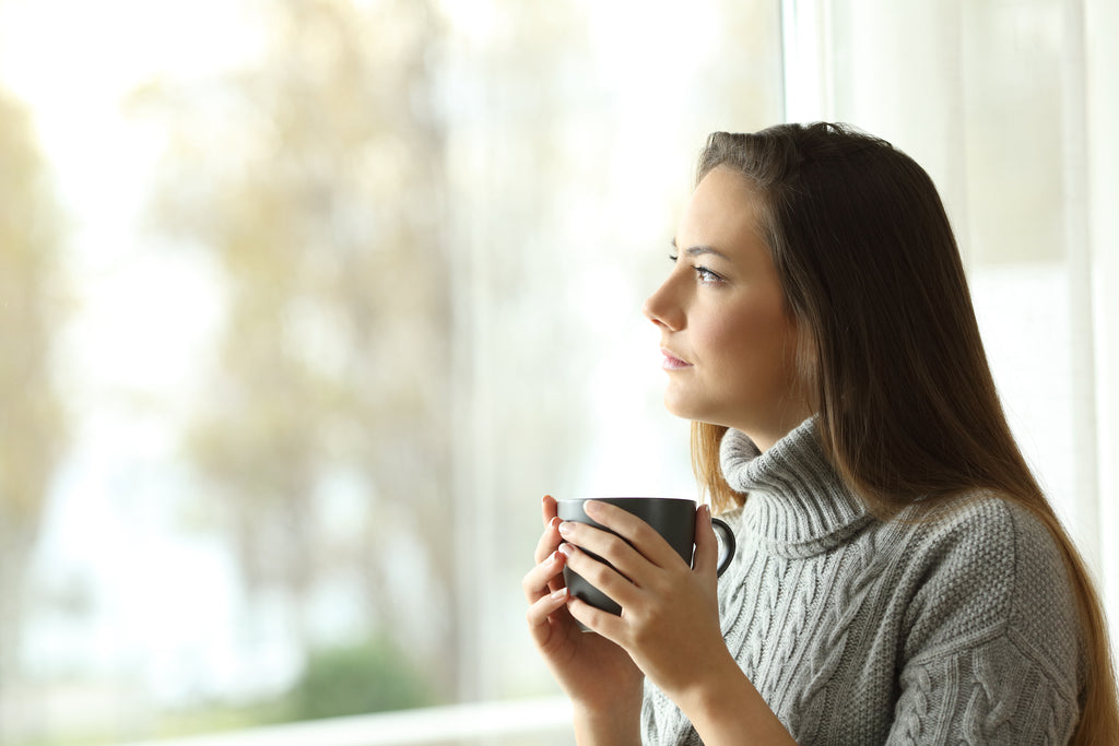 Caucasian woman looks out of the window thoughtfully with a cup in her hands