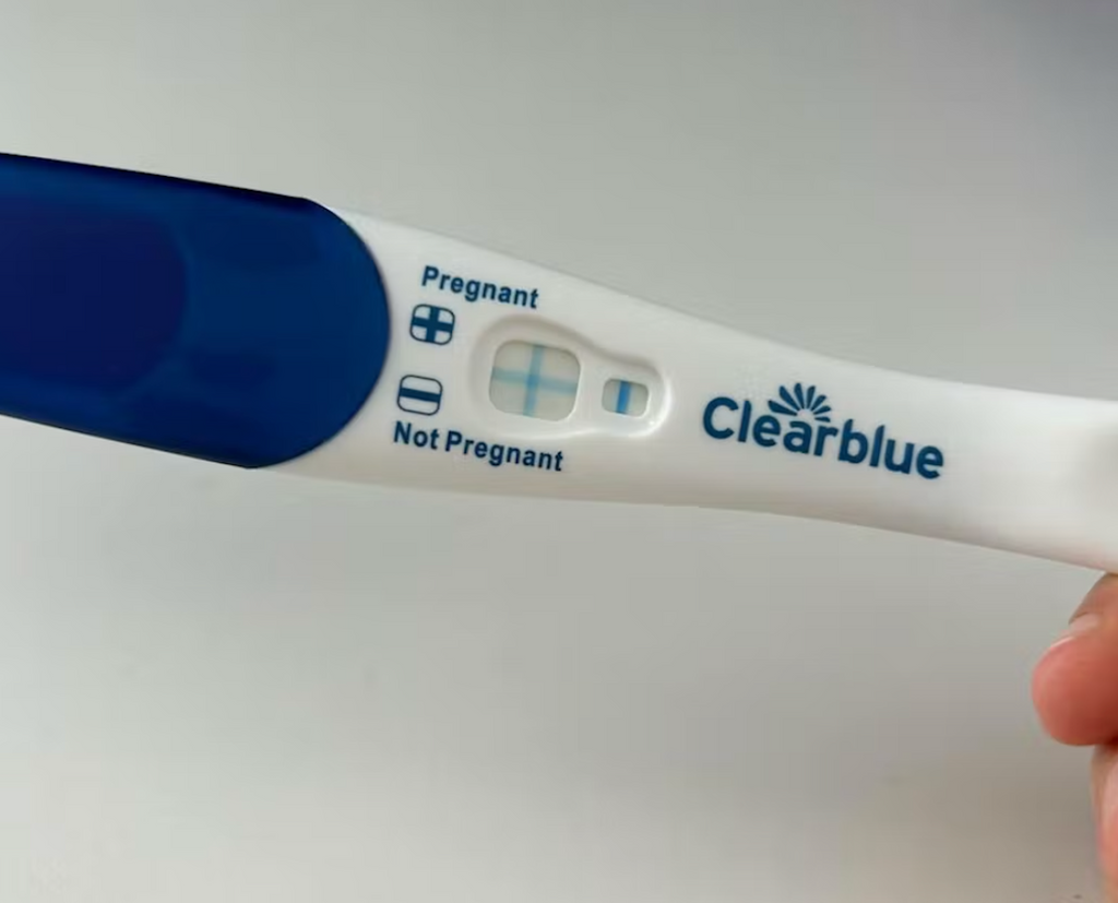 Rachel holds positive pregnancy test result with her hand