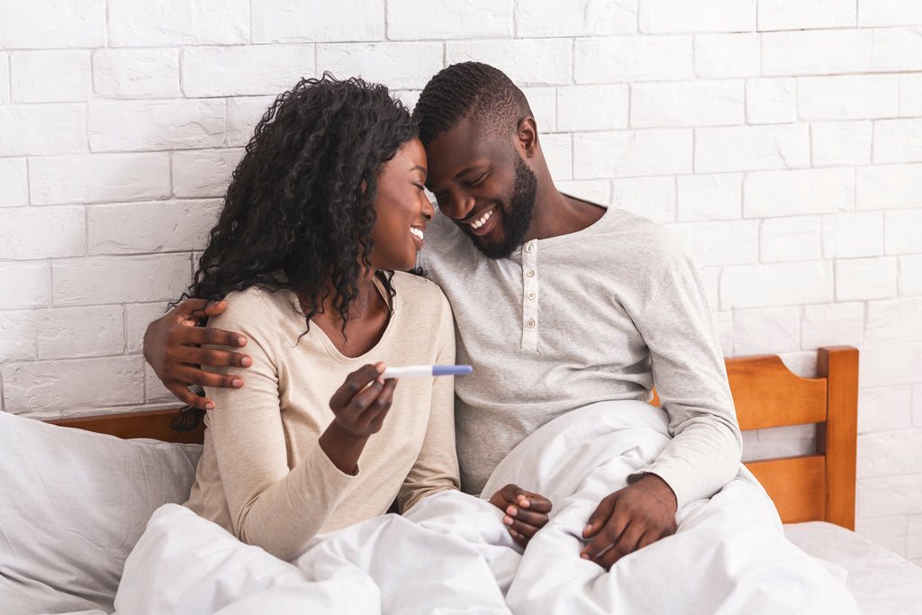 a black couple happy about their pregnancy test result in bed