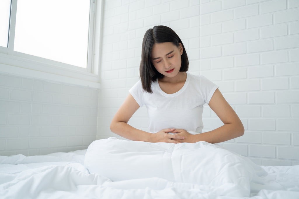 asian woman sits up in bed with pain in lower abdomen