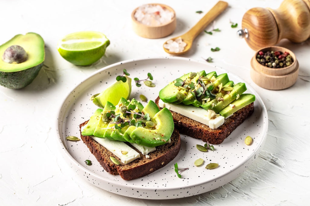 avocado toast on white plate with avocados and condiments in background