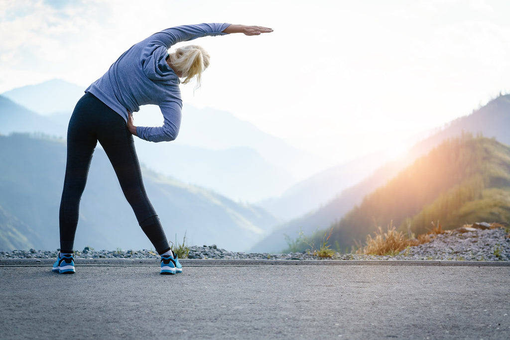 woman stretches sideways in front of mountain view