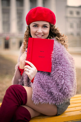 Woman wearing a purple capelet and over-the-knee boots while smiling and holding a red book