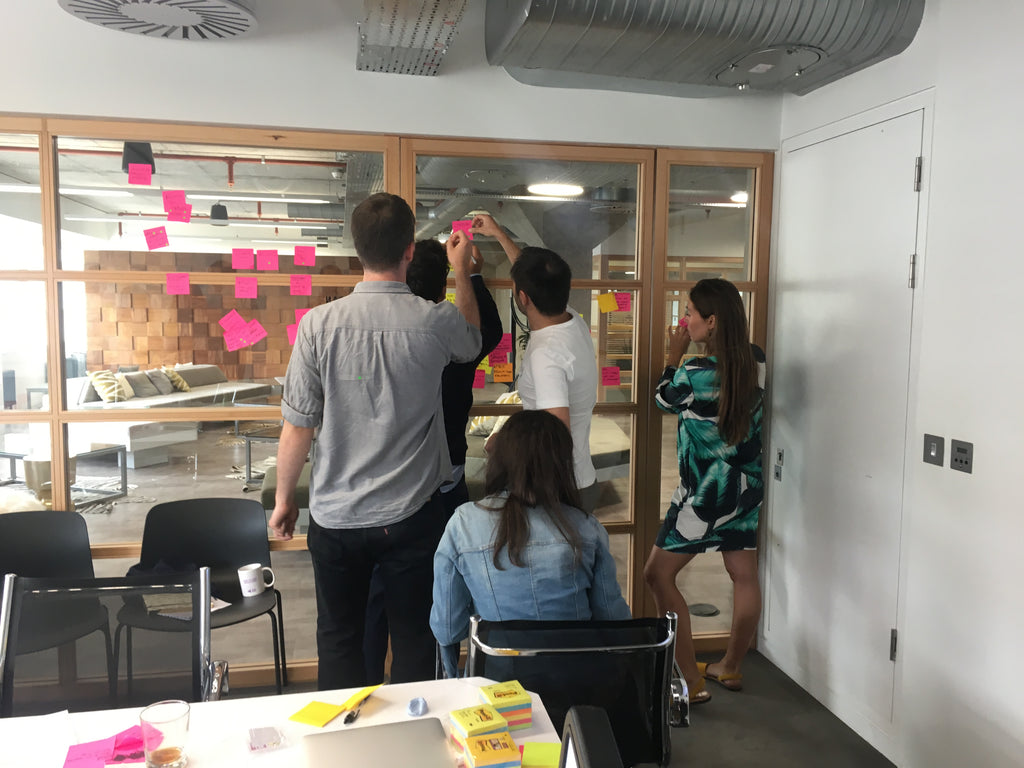 Product design workshop at Farfetch; team members placing clusters of post its on a wall and discussing