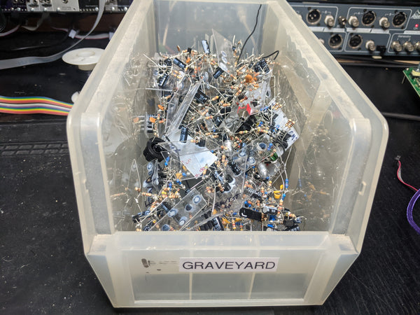 A clear plastic bin full of soldered through-hole components with a label that says "GRAVEYARD"