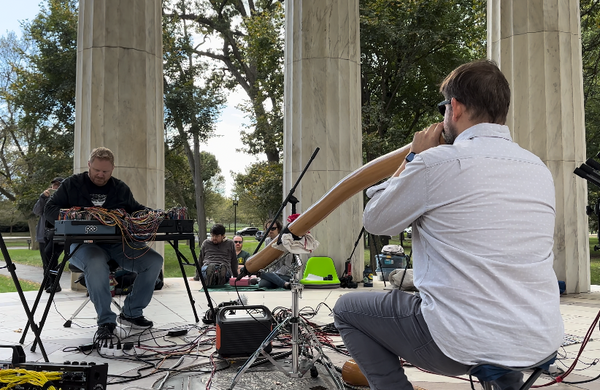 Patrick playing his modular and Gabe playing didgeridoo outside surrounded by stone columns at the Modular on the Mall show