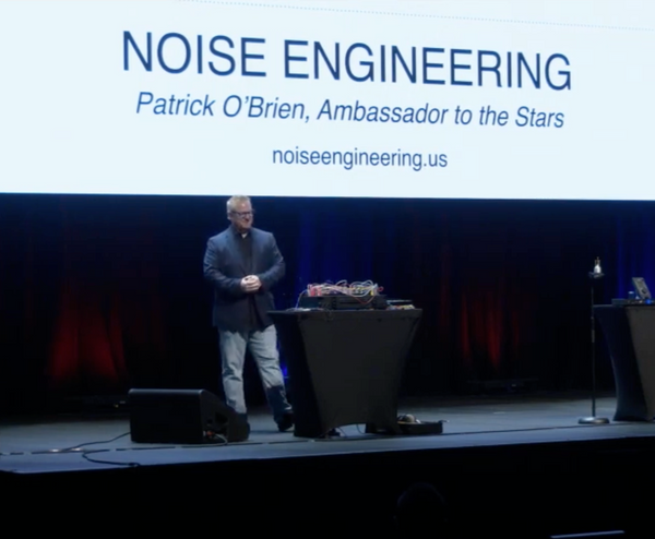 Patrick on stage at Sweetwater with a projector screen that says "NOISE ENGINEERING Patrick O'Brien, Ambassador to the Stars"