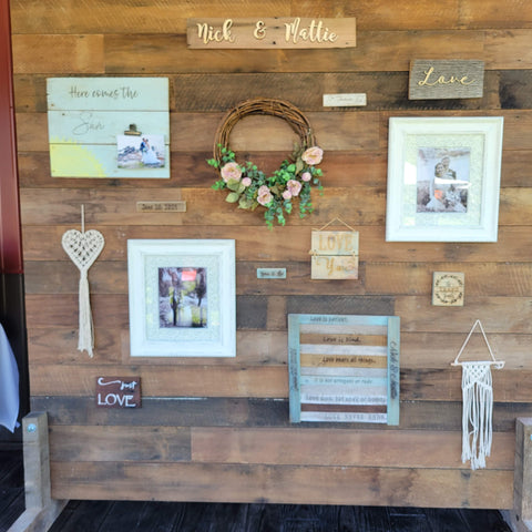 A freestanding pallet wood gallery wall. Laser engraved barn wood, "love you," rose grapevine wreath, macramé wall hangings, "here comes the sun," photographs.