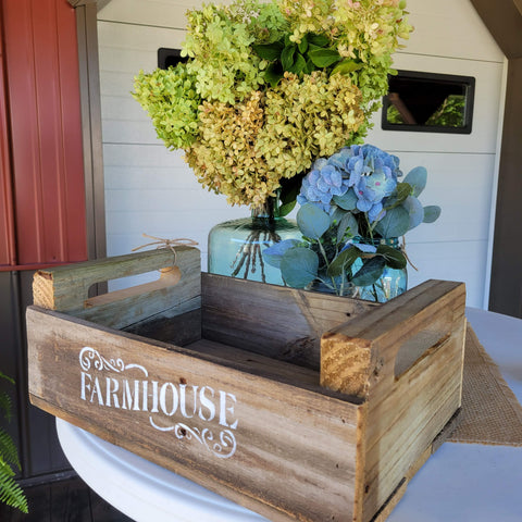 Handmade crate with Farmhouse stenciled on the front. Hydrangeas and eucalyptus in jars on a table.