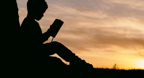 Child reading a book in silhouette with sunrise in the background