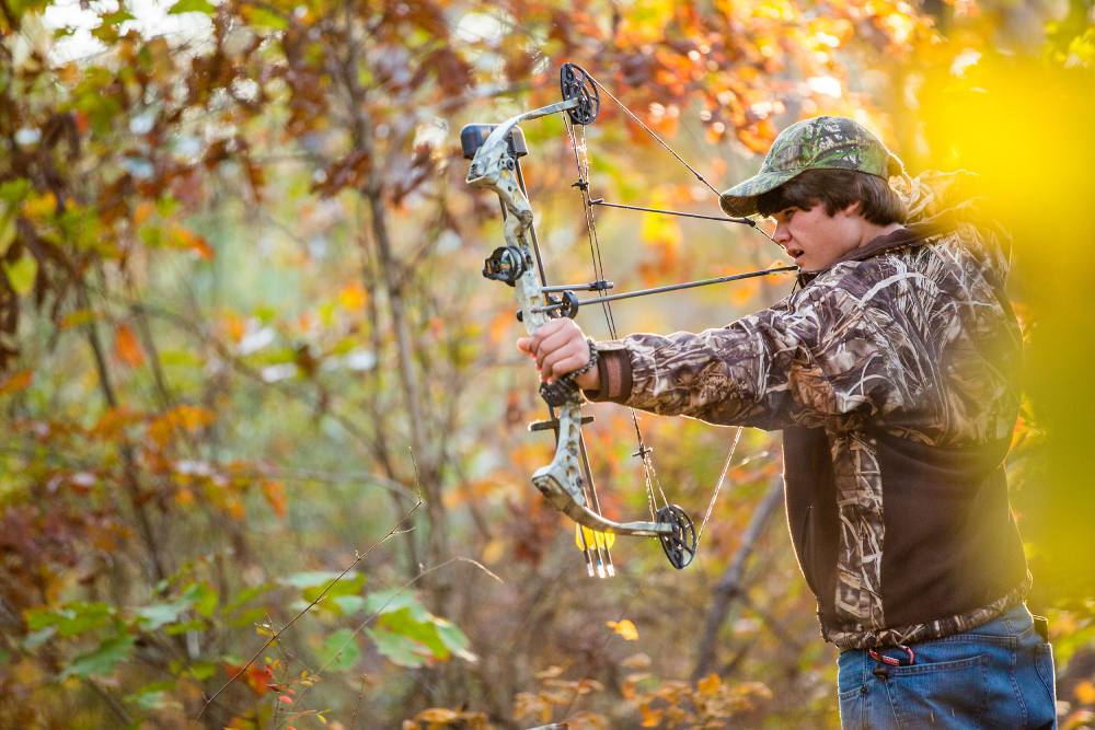 A boy in the woods shooting a compound bow