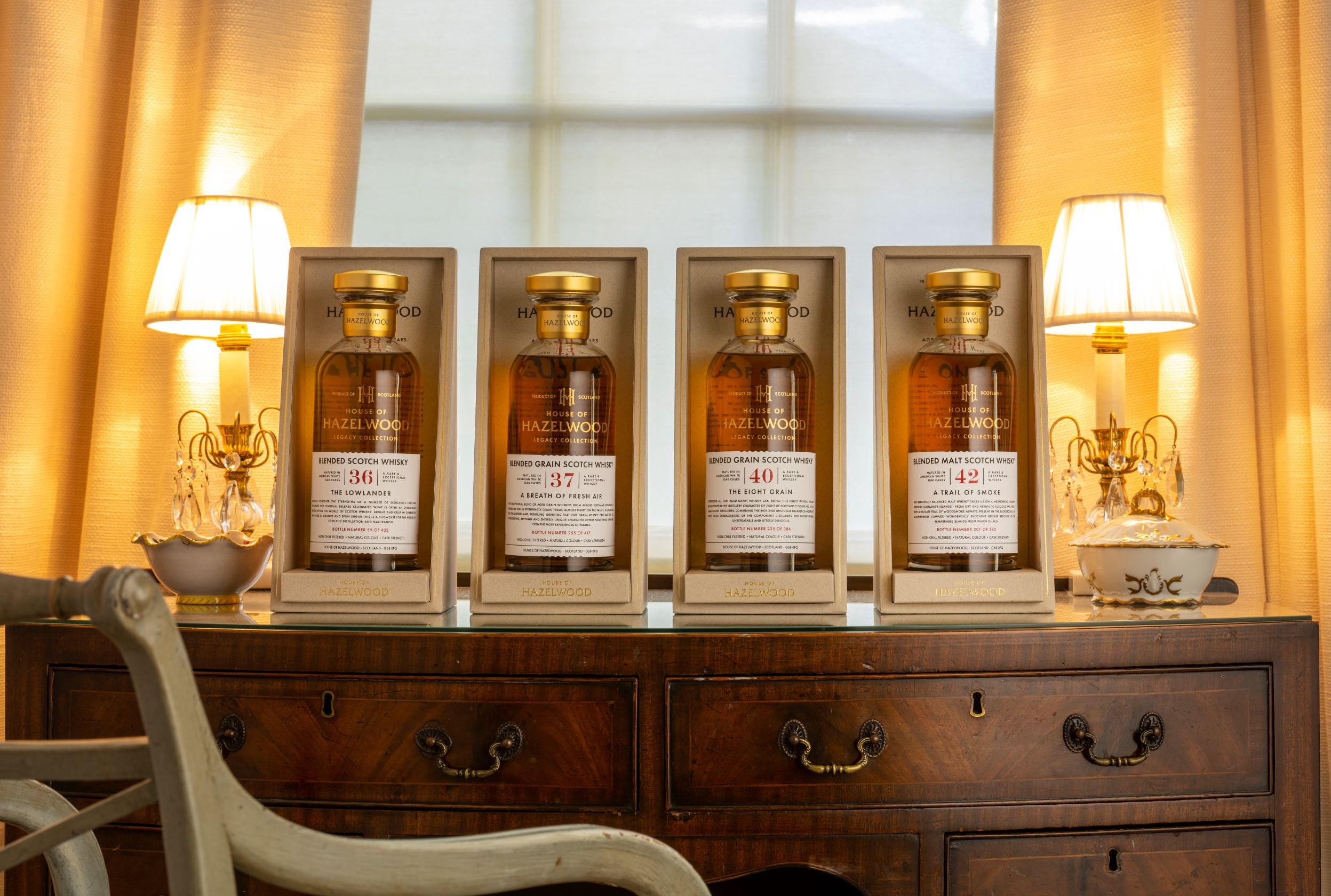 Four bottles of The Legacy Collection sitting on top of a dresser between to lamps.
