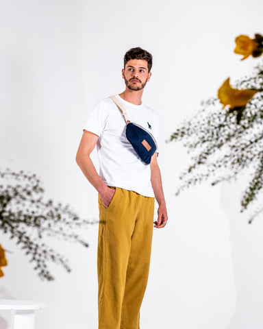 Tall man carrying navy blue fanny pack in white background with flower in foreground